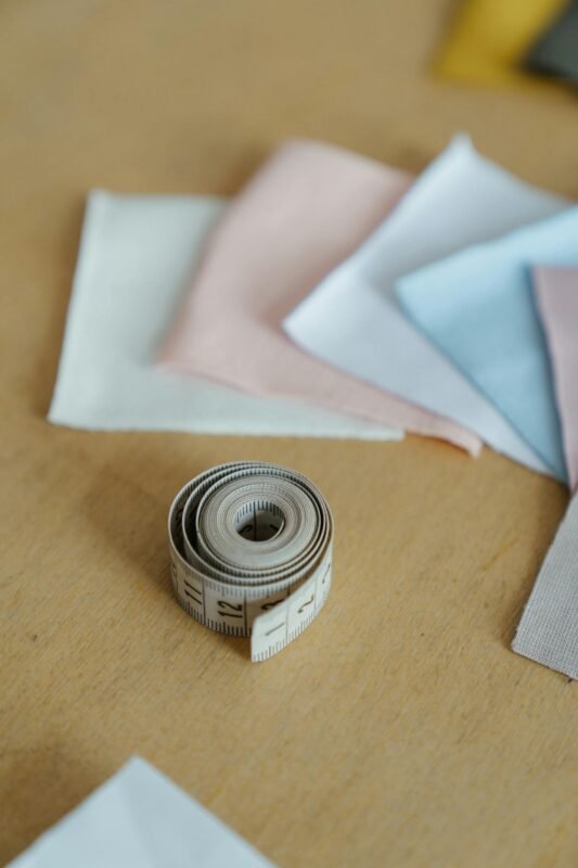 Close-up of vibrant fabrics and a rolled measuring tape on a wooden table in a workshop setting.