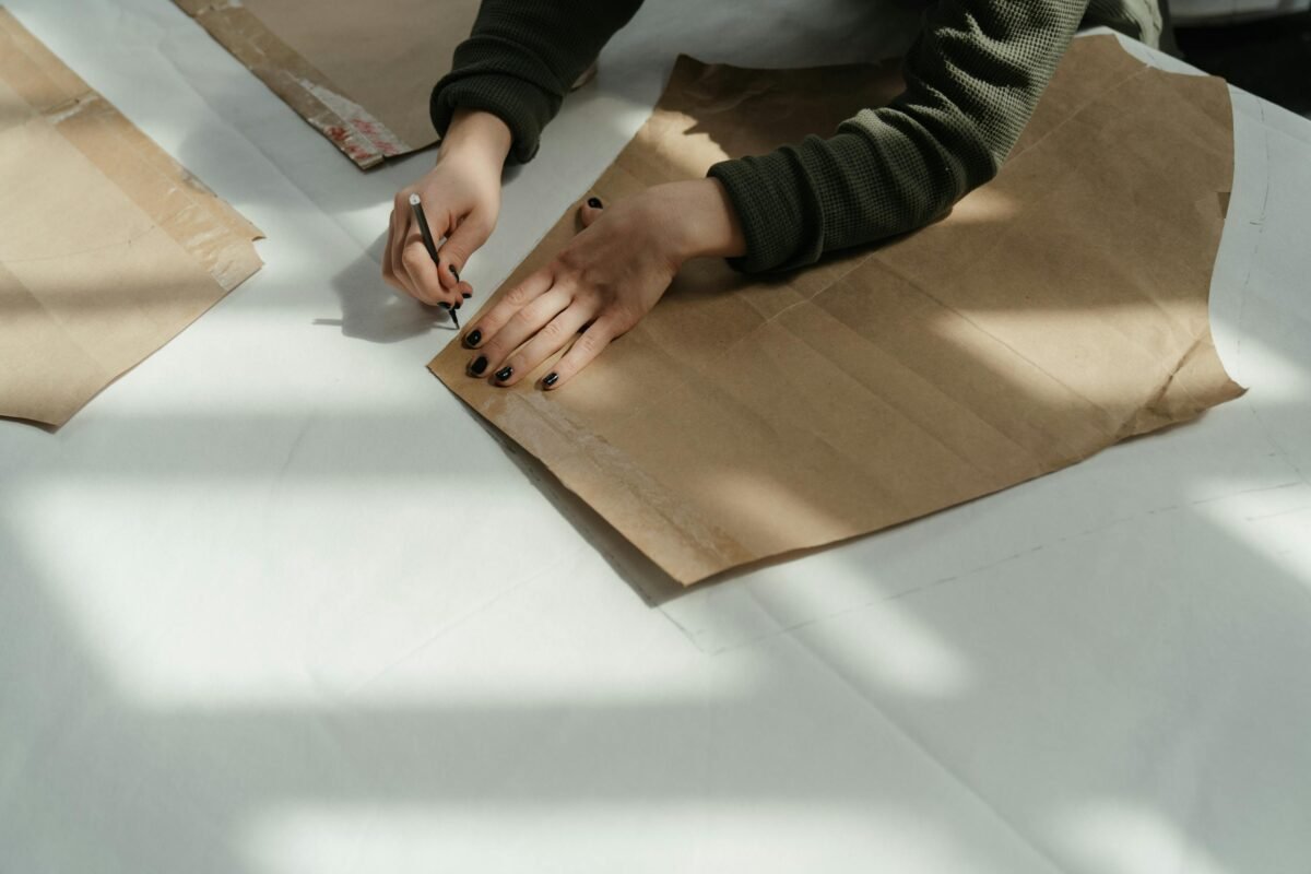 Tailor tracing patterns on brown paper in a sunlit workshop, capturing the art of fashion design.